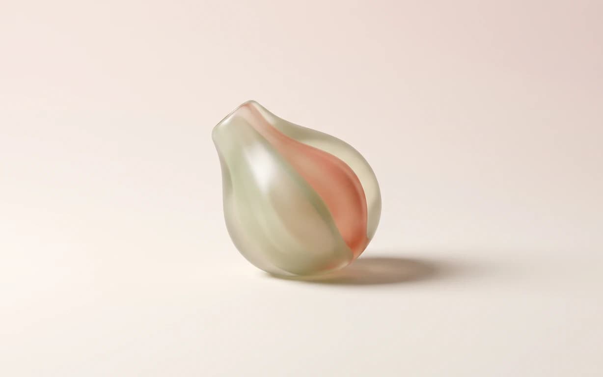 A translucent abstract sculpture in pale sage and coral rests on a warm ivory surface, casting a soft directional shadow.