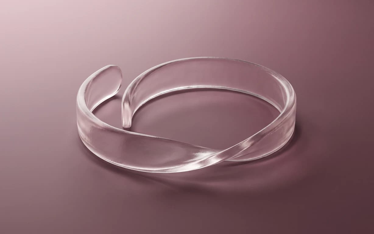 A translucent, ribbon-like loop rests on a muted plum surface under soft studio lighting.
