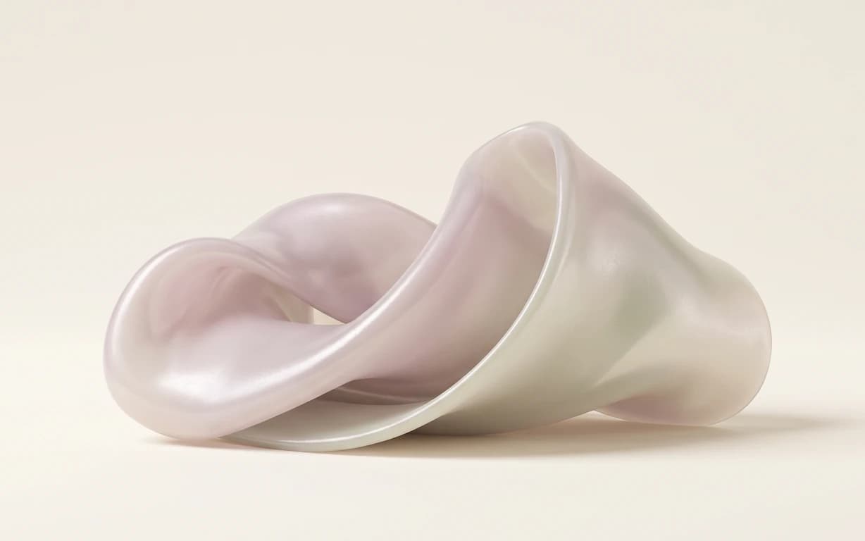 A softly iridescent, translucent folded sculpture in blush and ivory tones rests on a warm seamless surface.