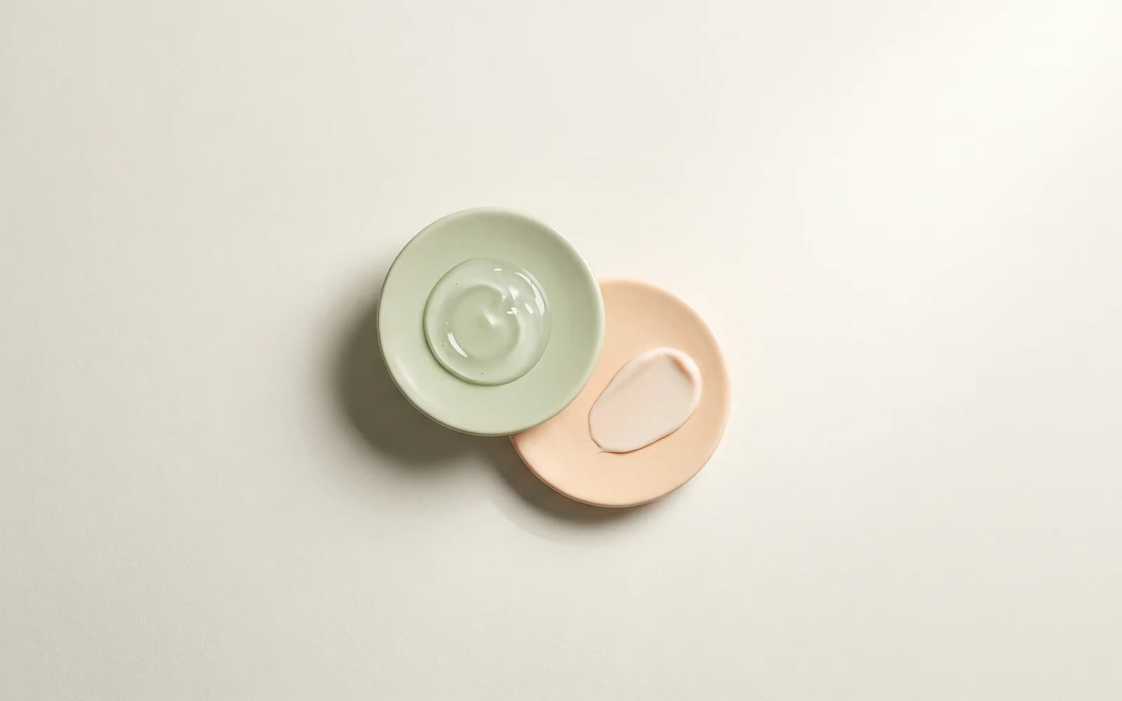Overlapping sage and peach ceramic discs holding gel and cream textures.