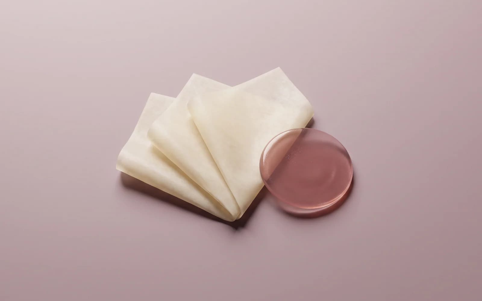 Soft ivory film pleats beside a translucent rose gel lens on pale plum.
