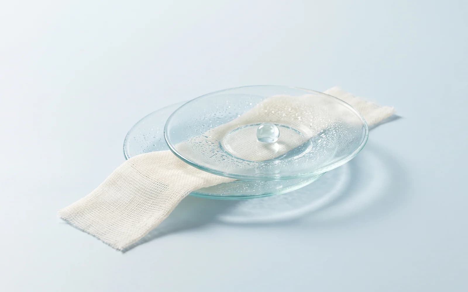 Offset clear glass saucers with condensation and a gel bead above ivory gauze.