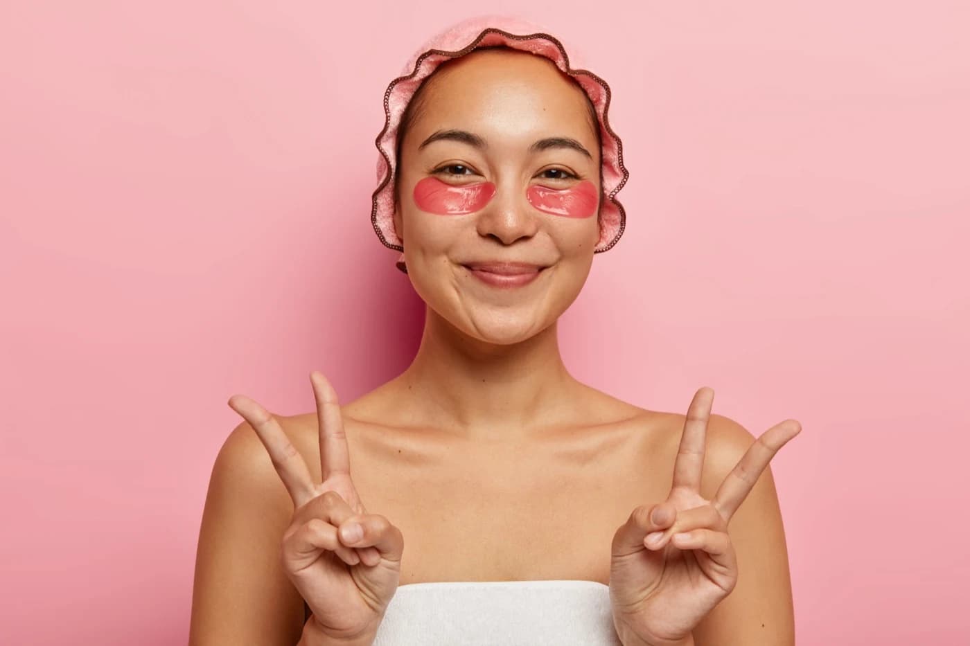 Smiling woman wearing pink under-eye patches and making peace signs