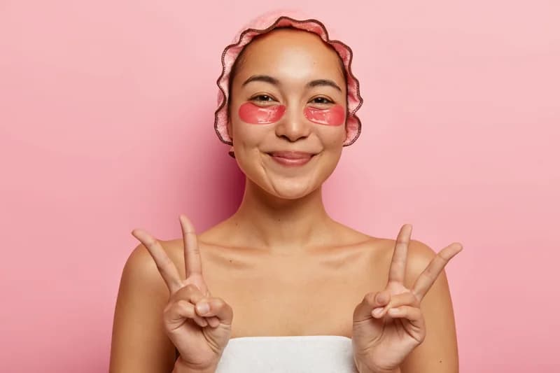 A smiling woman wearing pink under-eye patches during her skincare routine