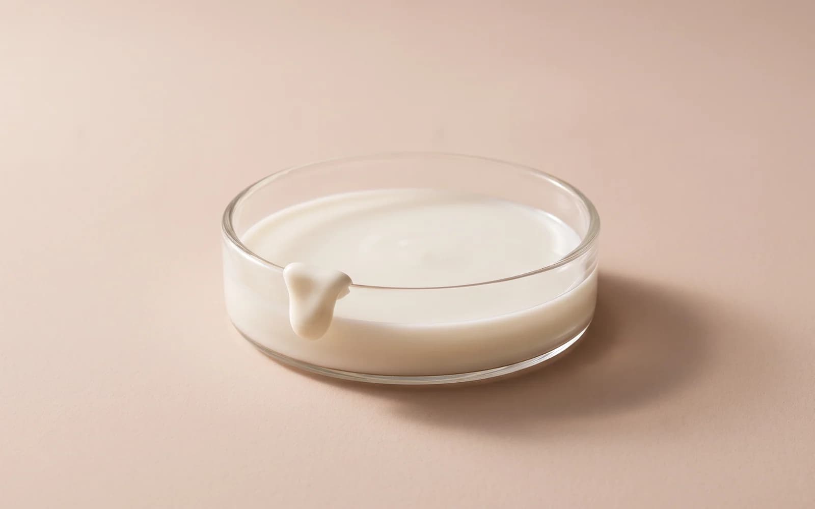 Milky white emulsion in a shallow glass dish with a small ivory form draped over the rim.