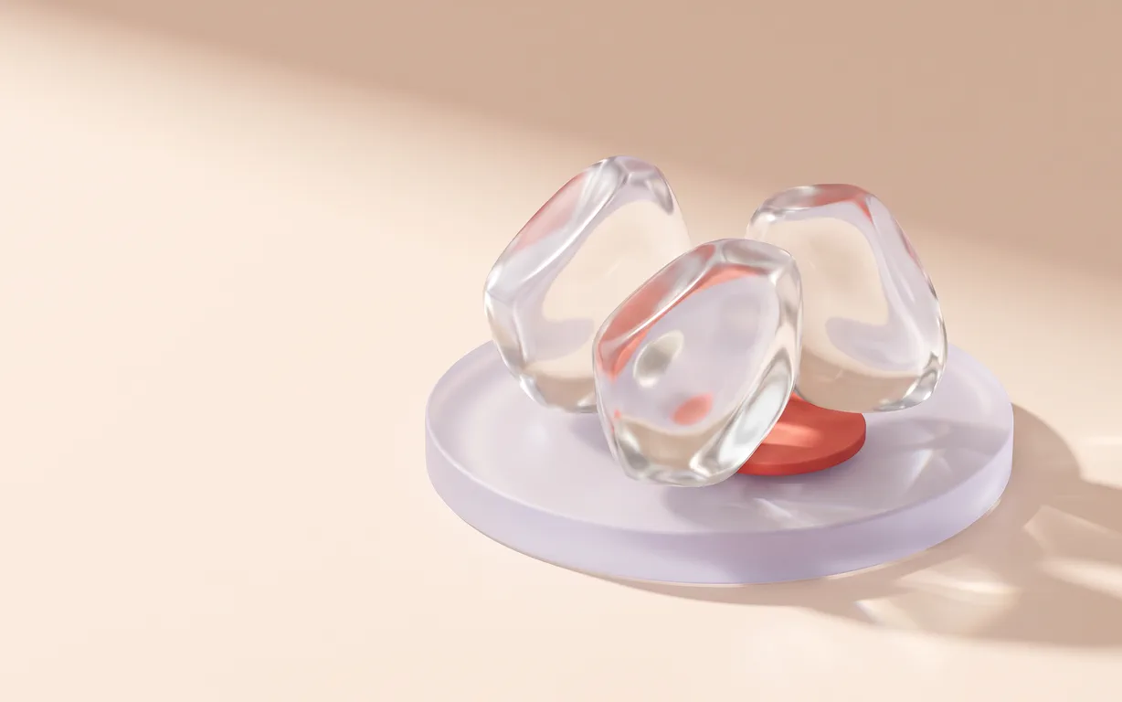 Three oversized translucent, softly faceted glass crystals arranged on a pale lavender stage above a blush background with a small coral accent.