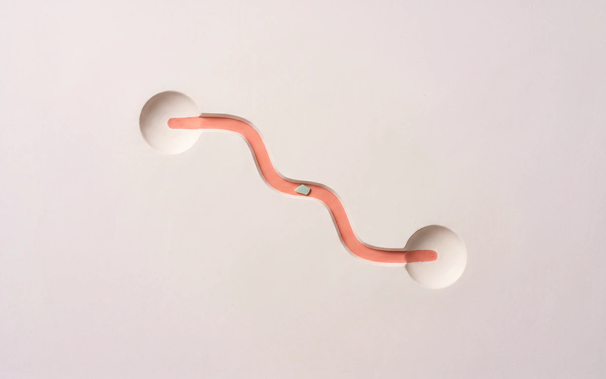 Two shallow plaster wells are joined by a winding coral relief path with one small celadon accent.