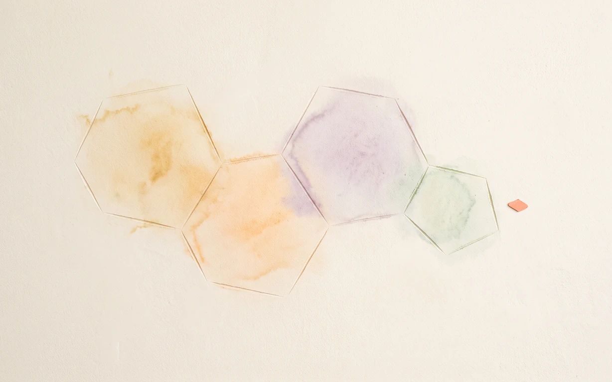 Four fused amber, apricot, lavender and celadon ring outlines form a flat steroid-like pattern on warm-ivory plaster beside a tiny coral diamond.