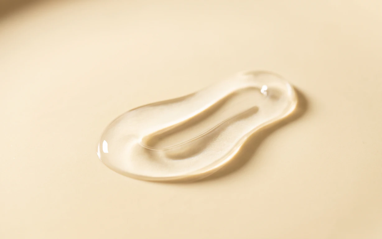 Clear, glossy glycerin-inspired liquid folded on a pale buttercream surface.