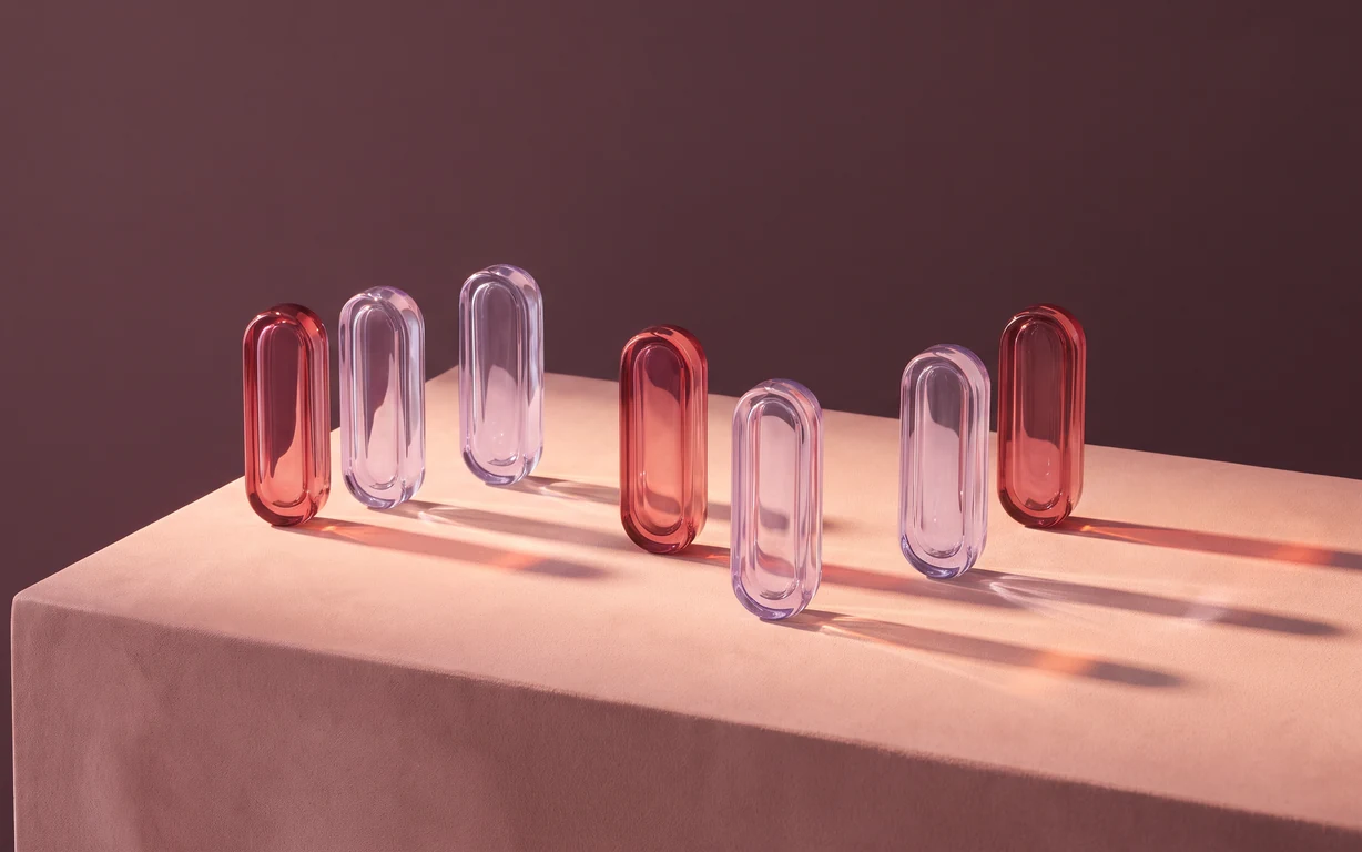 Seven rose and lilac glass lozenges form a loose sequence across a blush pedestal against a muted plum backdrop.