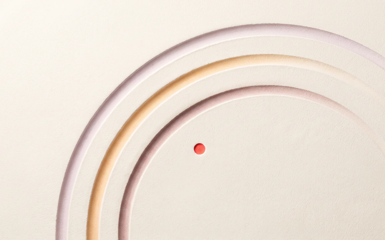 Three open mauve, apricot and auburn grooves arc across one warm-ivory matte plaster surface beside a tiny coral point.