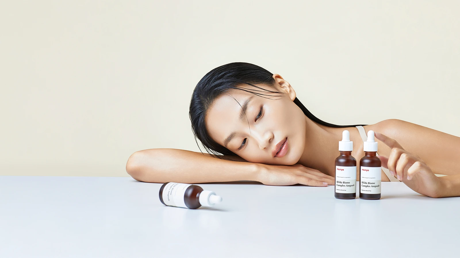 Woman resting beside ma:nyo skincare ampoules